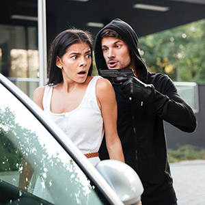 Aggressive man thief in gloves threatening with gun to frightened young woman on car parking